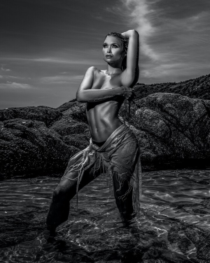 Woman posing in shallow rocky seawater in a dramatic black-and-white fine-art portrait