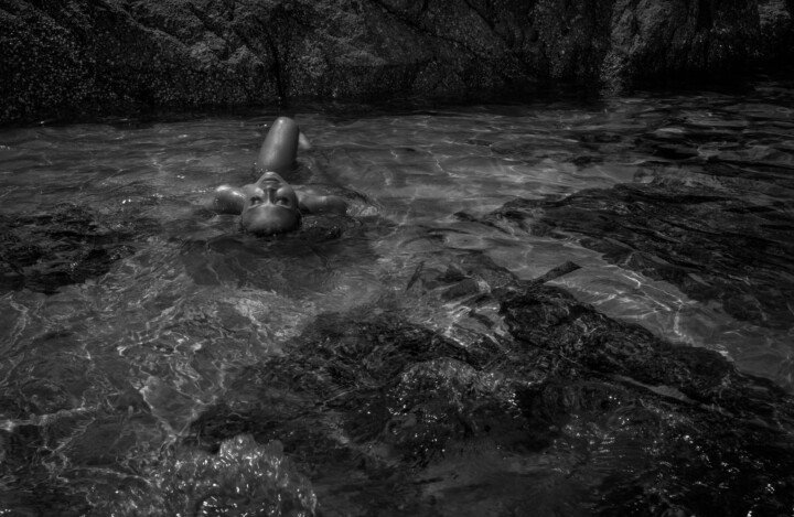 Woman floating in shallow rocky seawater in a wide black-and-white fine-art photograph