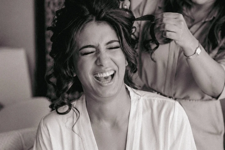 A joyful bridal preparation moment as the bride laughs while having her hair styled.