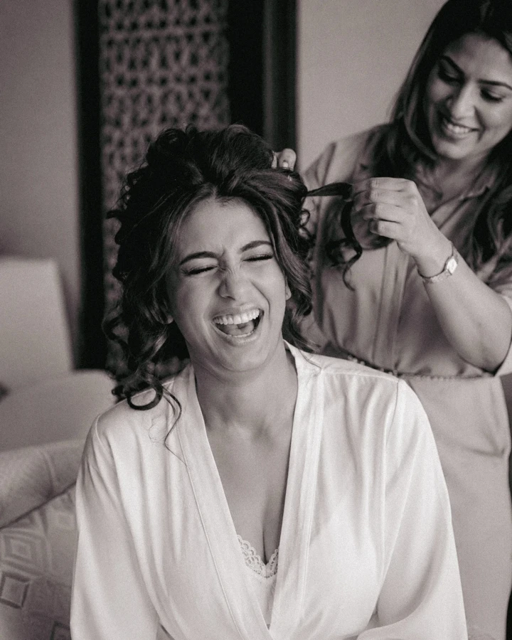 A joyful bridal preparation moment as the bride laughs while having her hair styled.
