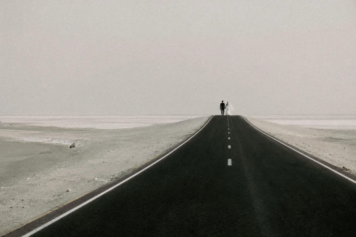 Bride and groom standing together on a long empty road in the Abu Dhabi desert.