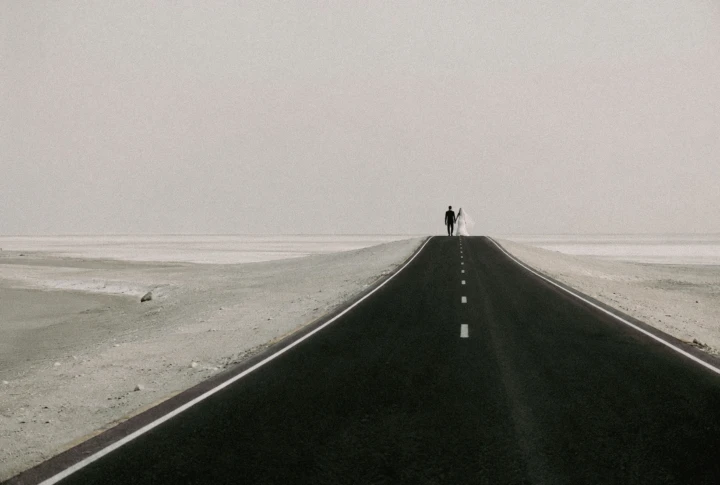 Bride and groom standing together on a long empty road in the Abu Dhabi desert.