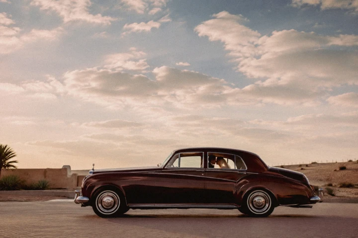 Bride and groom sitting inside a vintage luxury car during a desert wedding in Abu Dhabi.