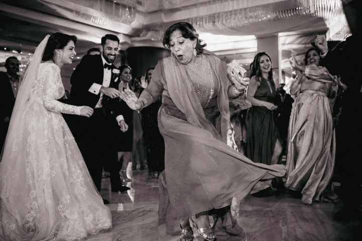 Bride, groom and wedding guests laughing as a woman dances at an Abu Dhabi wedding reception.