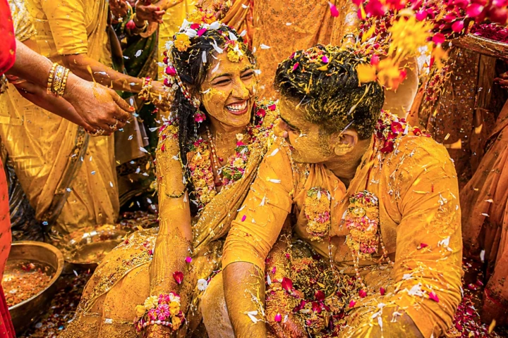 Indian bride and groom laughing while covered with turmeric and flower petals during a colorful Haldi ceremony in Dubai.