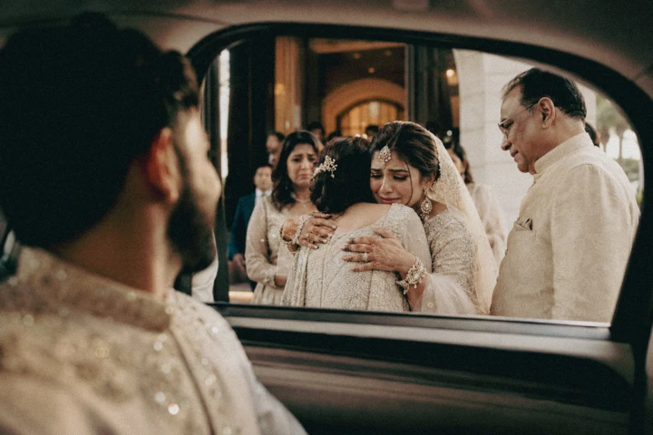 Emotional Indian bride hugging a family member beside a wedding car during her Vidaai in Dubai.