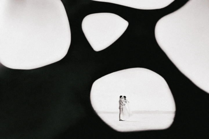 Bride and groom framed through an abstract dark foreground during a creative desert wedding portrait in Abu Dhabi.