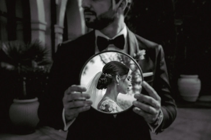 Groom holding a round mirror reflecting the bride during a creative wedding portrait in Dubai.