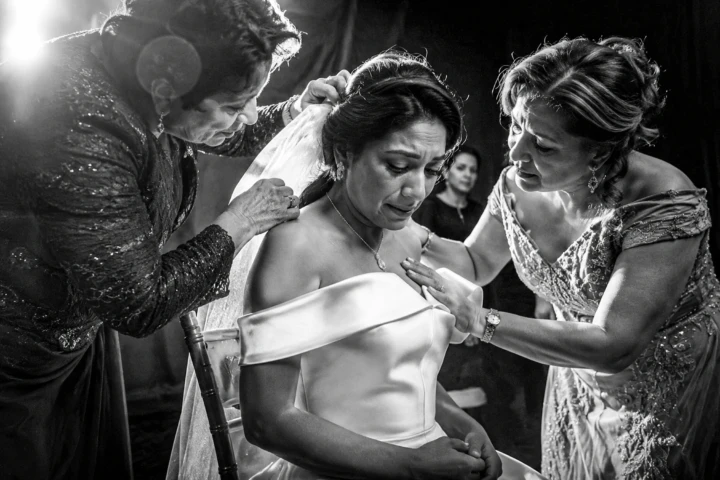 Emotional Afghan bride seated as two family members adjust her veil before a wedding in Dubai