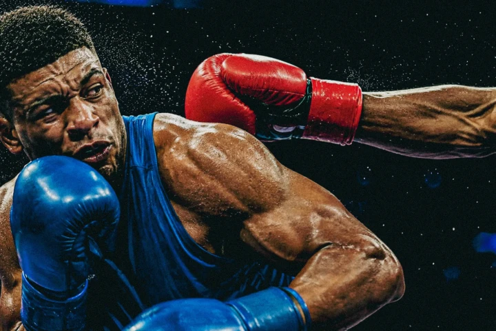 Boxer in blue gloves taking a punch during a professional boxing match in Dubai