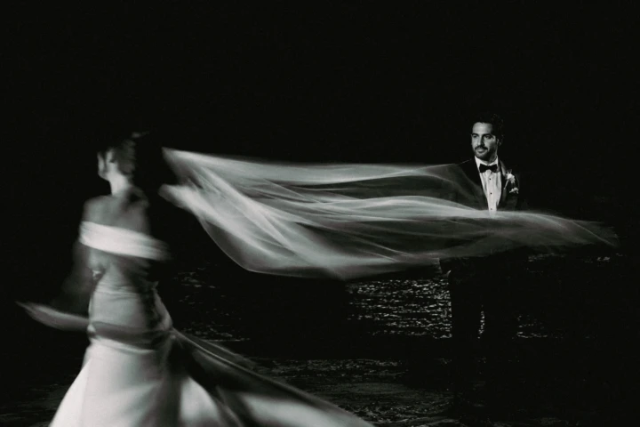 Bride moving through the frame as her flowing veil leads toward the groom during a night wedding portrait in Dubai.
