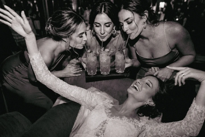 Laughing bride surrounded by bridesmaids drinking cocktails at a wedding reception in Dubai.