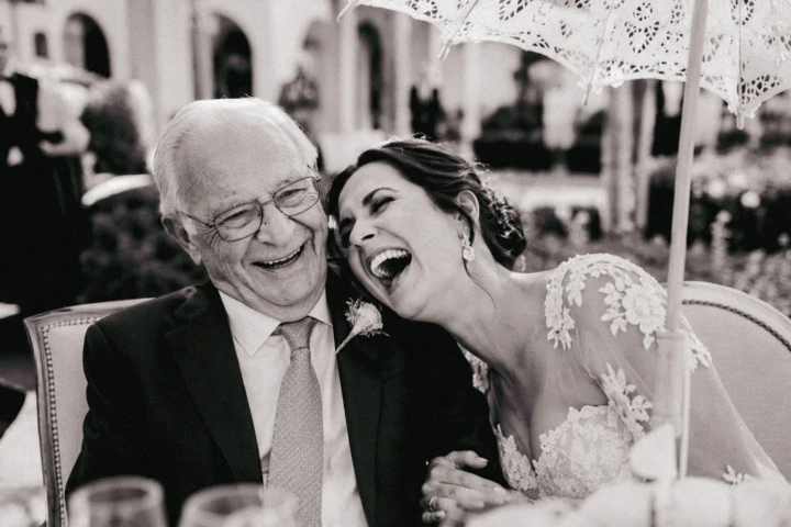 Bride laughing with an elderly family member beneath a parasol at an outdoor wedding in Dubai.