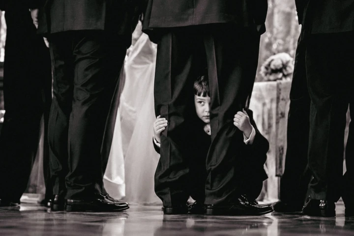 Young child peeking between the legs of groomsmen dressed in black suits at a Dubai wedding.