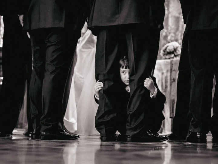 Young child peeking between the legs of groomsmen dressed in black suits at a Dubai wedding.