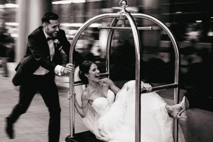 Groom pushing a laughing bride seated on a hotel luggage cart during their wedding in Dubai.