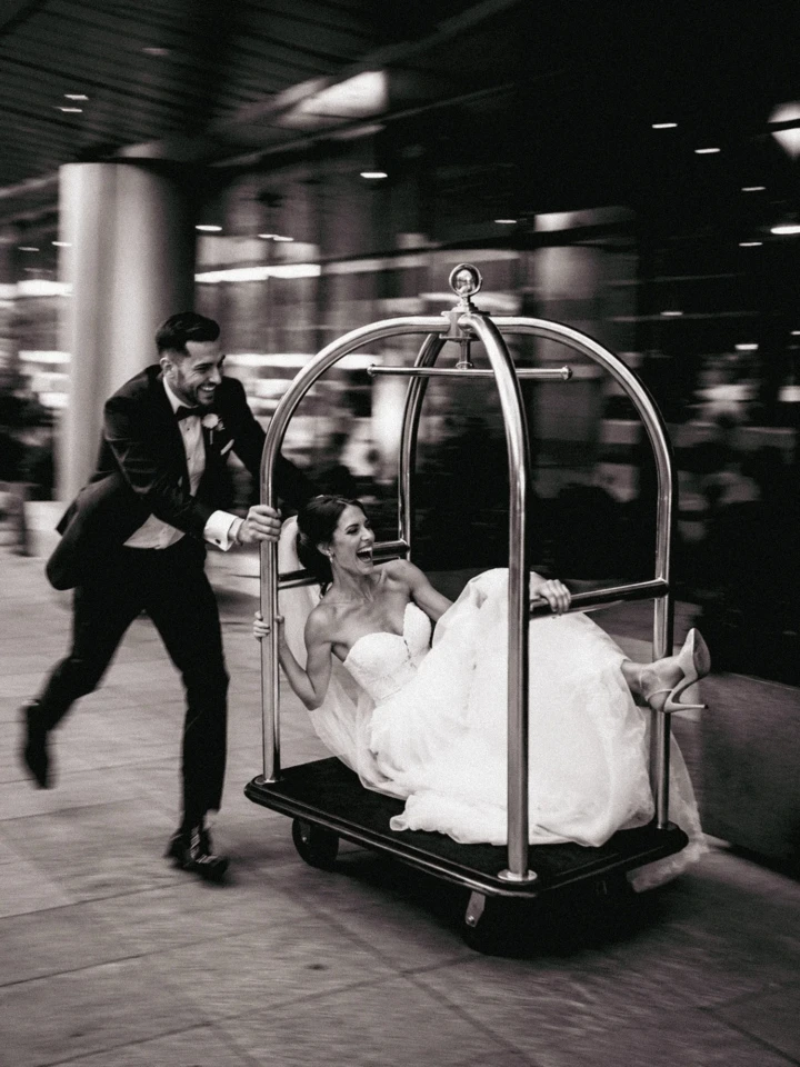 Groom pushing a laughing bride seated on a hotel luggage cart during their wedding in Dubai.