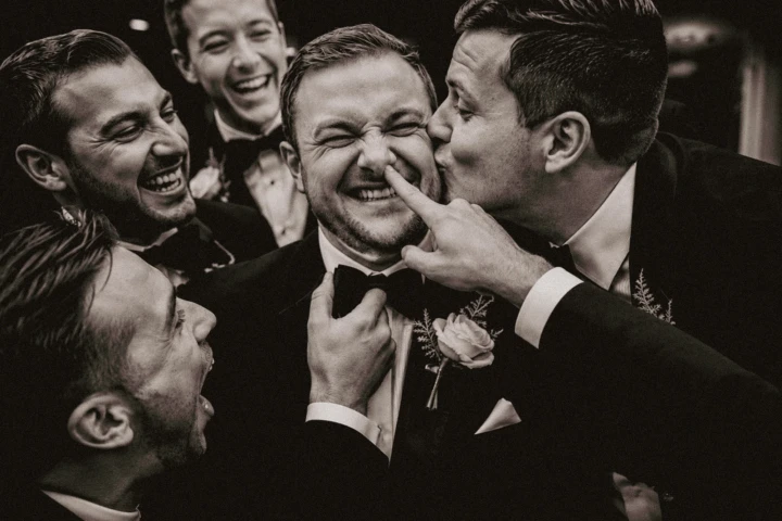 Laughing groomsmen kissing and teasing their friend during a candid wedding moment in Dubai.
