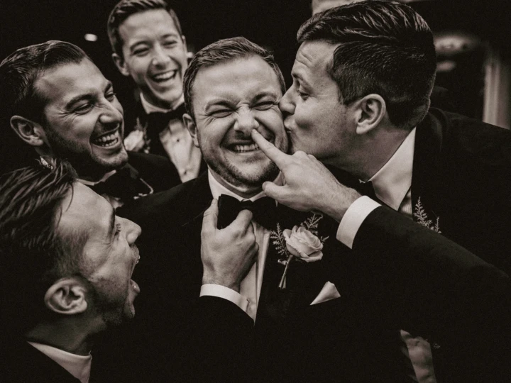 Laughing groomsmen kissing and teasing their friend during a candid wedding moment in Dubai.