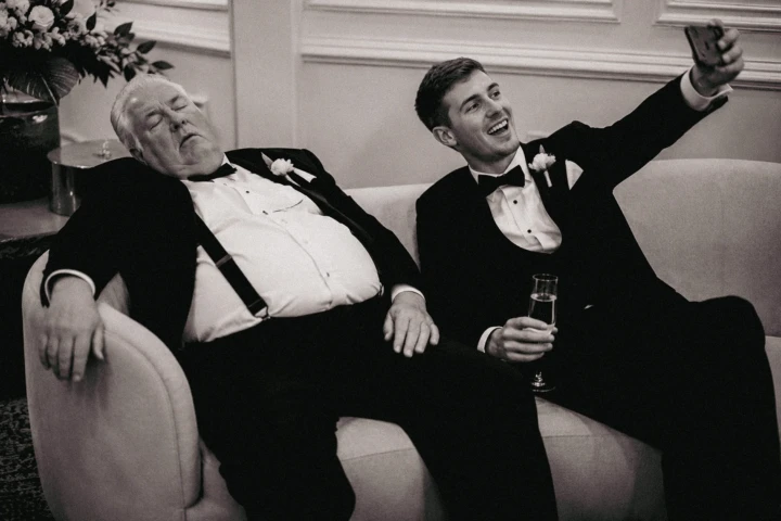 Wedding guest taking a selfie beside an older man sleeping on a sofa at a luxury wedding in Dubai.