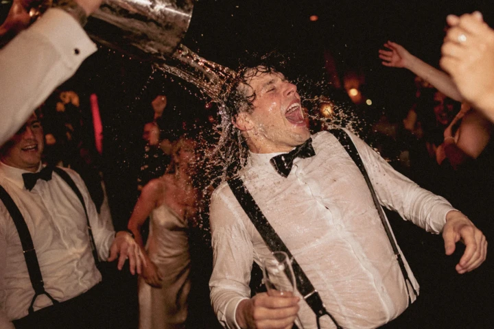Laughing groom being splashed with water by friends during a lively wedding reception in Dubai.