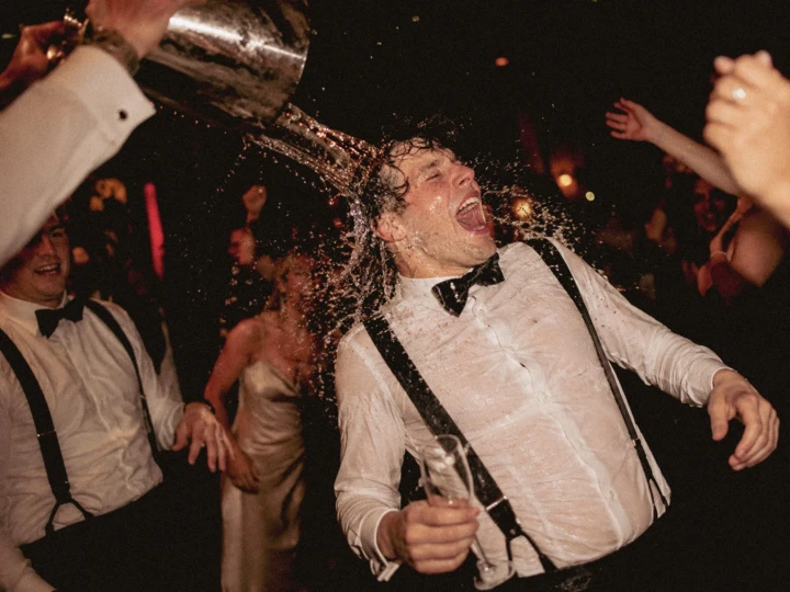 Laughing groom being splashed with water by friends during a lively wedding reception in Dubai.