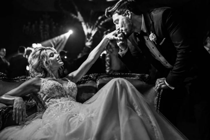Groom kissing the bride’s hand as she sits on an elegant sofa during a black-and-white Istanbul wedding portrait.