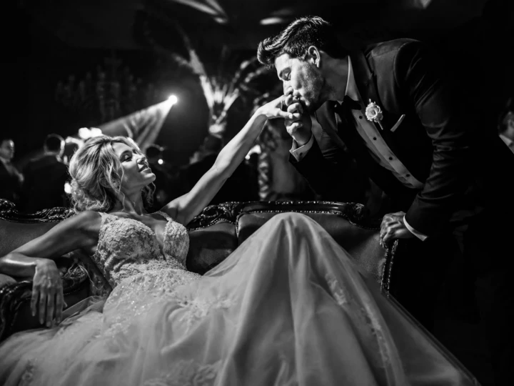 Groom kissing the bride’s hand as she sits on an elegant sofa during a black-and-white Istanbul wedding portrait.