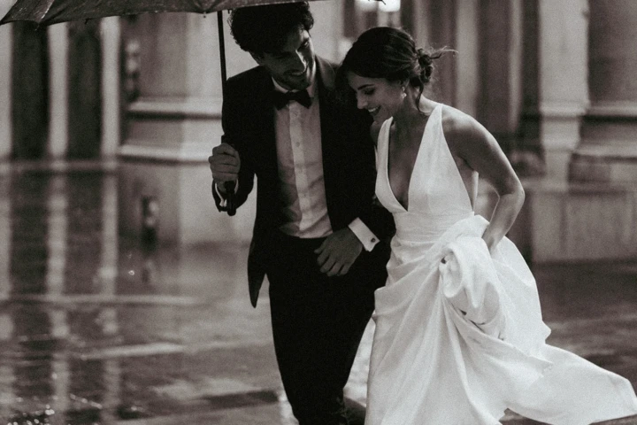 Bride and groom walking beneath a black umbrella in the rain outside an elegant Istanbul wedding venue.