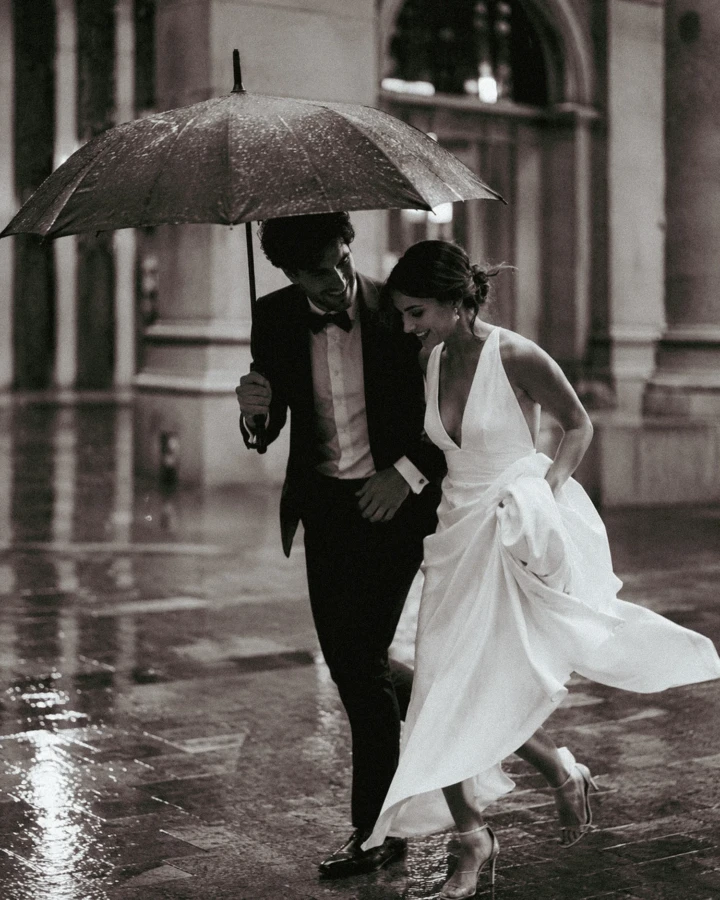 Bride and groom walking beneath a black umbrella in the rain outside an elegant Istanbul wedding venue.