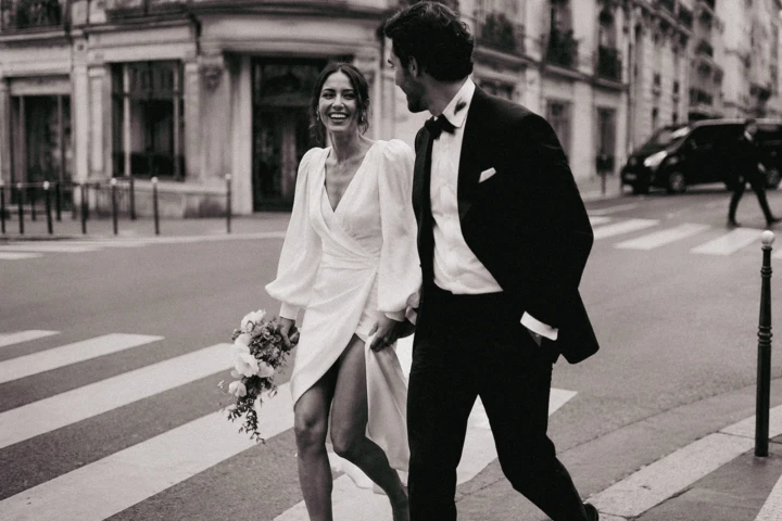Bride holding a bouquet and laughing with the groom while walking across a street in Istanbul.