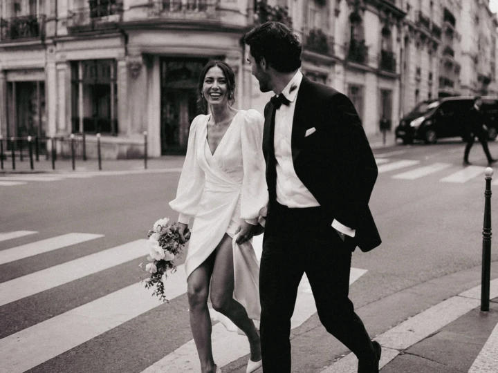 Bride holding a bouquet and laughing with the groom while walking across a street in Istanbul.