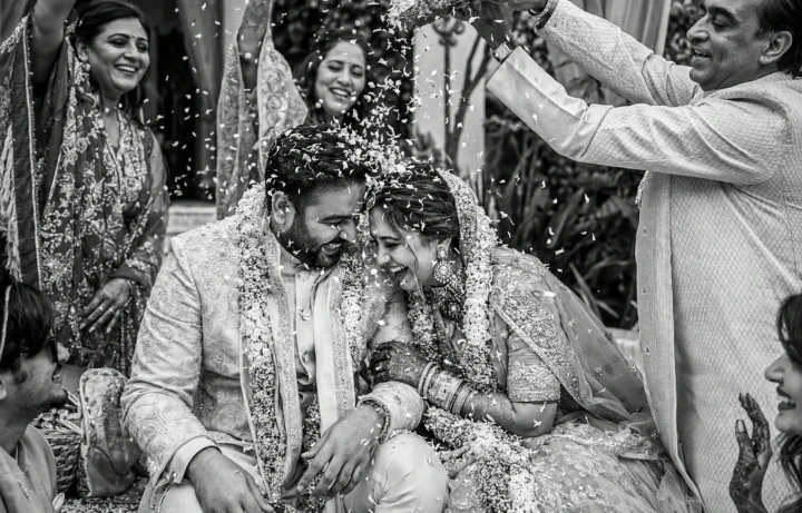 Indian bride and groom laughing while family members shower them with rice during a wedding ceremony in Dubai.