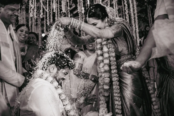 Indian bride pouring rice over the laughing groom during a traditional wedding ritual in Dubai.