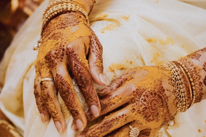 Indian bride’s hands decorated with intricate mehndi, gold bangles and turmeric during a Dubai wedding ceremony.