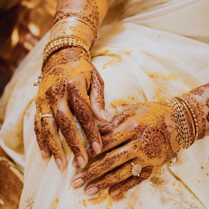Indian bride’s hands decorated with intricate mehndi, gold bangles and turmeric during a Dubai wedding ceremony.
