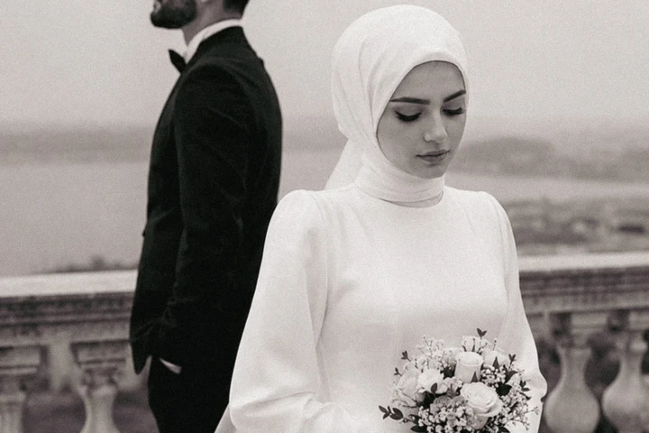 Bride and groom in the foreground with family members reflected in a mirror during a Muslim wedding ceremony in the UAE.