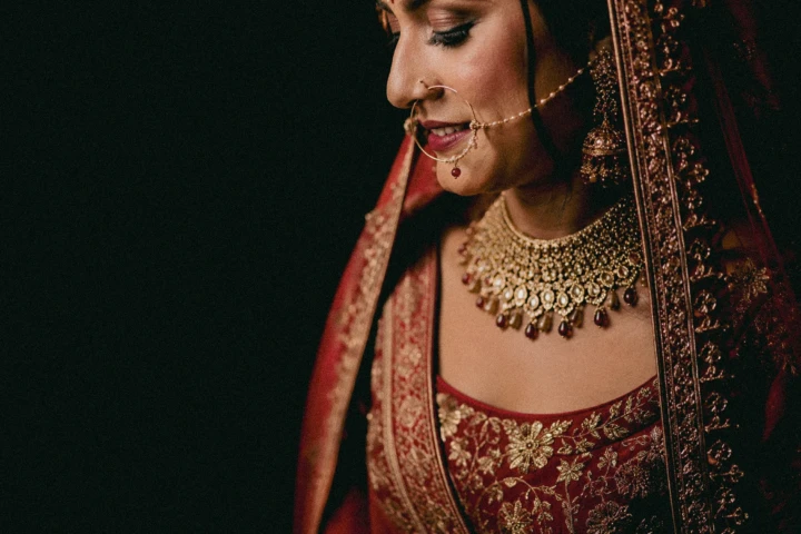 Indian bride wearing a red embroidered wedding outfit with traditional gold jewelry in Dubai.