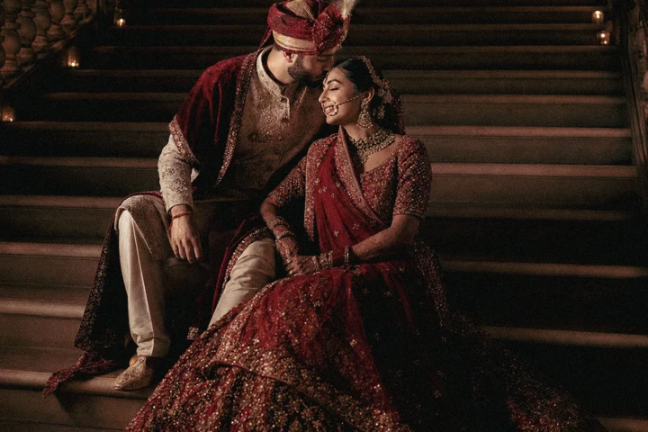 Indian bride and groom wearing red and gold wedding attire while seated on a grand staircase in Dubai.