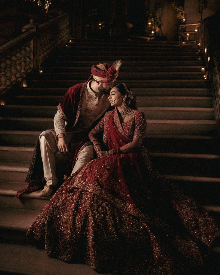 Indian bride and groom wearing red and gold wedding attire while seated on a grand staircase in Dubai.