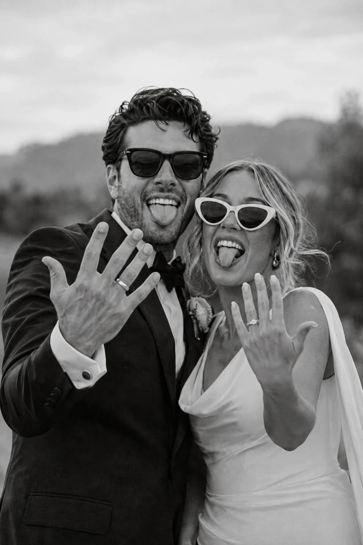 Bride and groom wearing sunglasses, showing their wedding rings and making playful expressions after the ceremony.