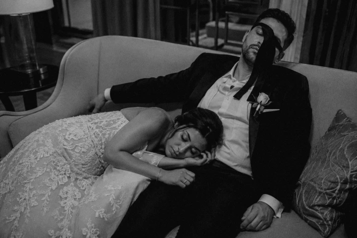 Tired bride and groom sleeping together on a sofa after their wedding celebration in the UAE.