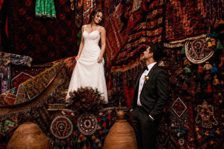 Bride and groom posing among colorful Turkish carpets and traditional textiles during a wedding portrait session in Turkey.