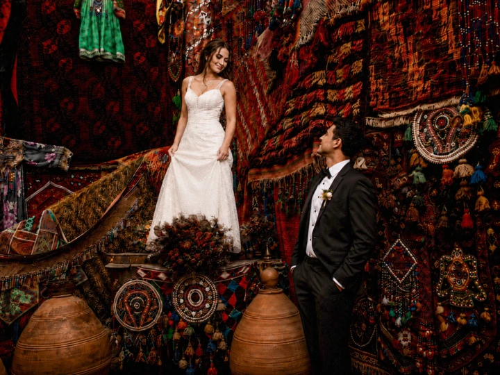 Bride and groom posing among colorful Turkish carpets and traditional textiles during a wedding portrait session in Turkey.