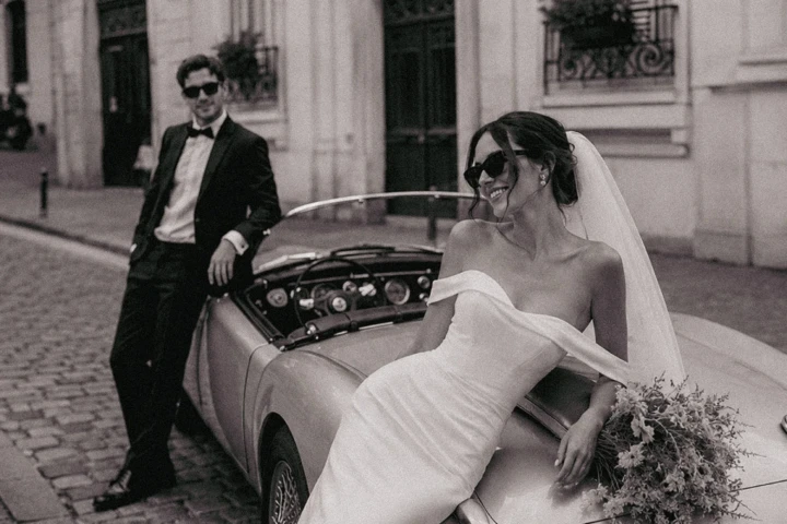 Bride sitting on a vintage convertible with the groom standing nearby on a historic cobblestone street in Turkey.