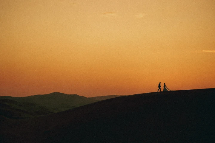 Silhouette of a bride and groom walking across desert dunes at sunset in the UAE.