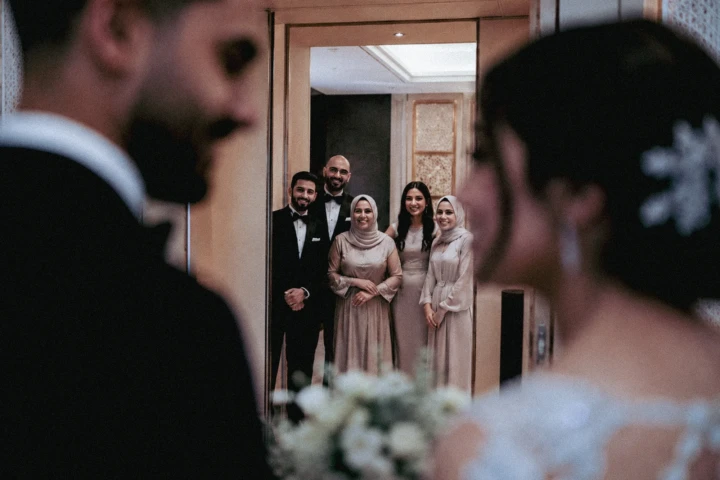 Bride and groom in the foreground with family members reflected in a mirror during a Muslim wedding ceremony in the UAE.