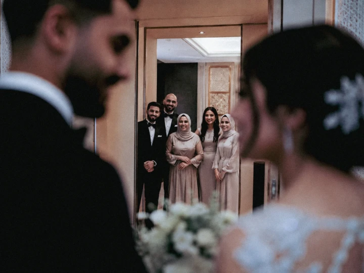 Bride and groom in the foreground with family members reflected in a mirror during a Muslim wedding ceremony in the UAE.