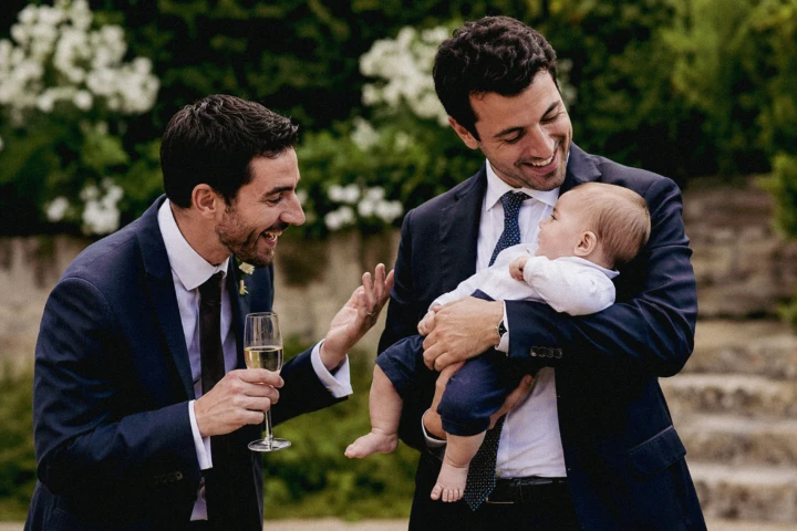 Two male wedding guests smiling and playing with a baby during an outdoor wedding celebration in the UAE.