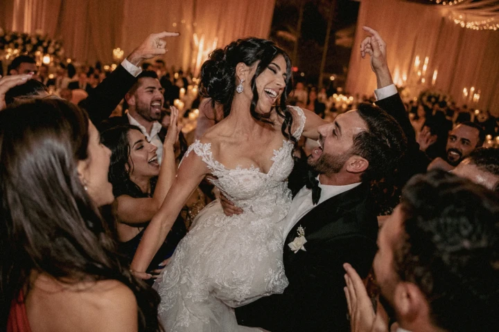 Laughing bride lifted by the groom while guests celebrate around them on a UAE wedding dance floor.